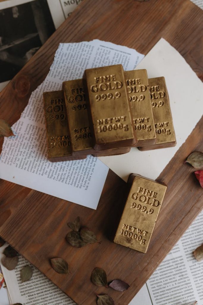 Pile of shiny gold bars engraved with fine gold purity, placed on a wooden board.